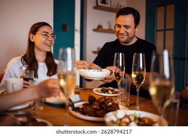 Una mujer joven y un hombre están bebiendo champán y comiendo en la sala de estar. Una feliz cena familiar. Un marido y su esposa están almorzando y riendo en una mesa. Encuentro de amigos