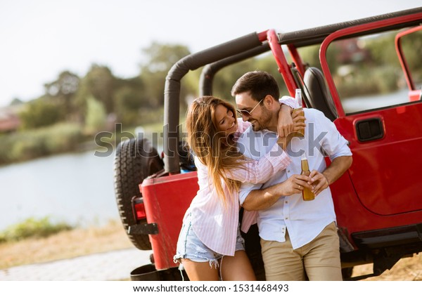 Young woman and man having fun outdoor near red car\
at hot summer day