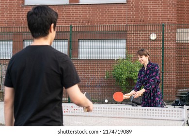 A Young Woman And A Man Playing Table Tennis Outside