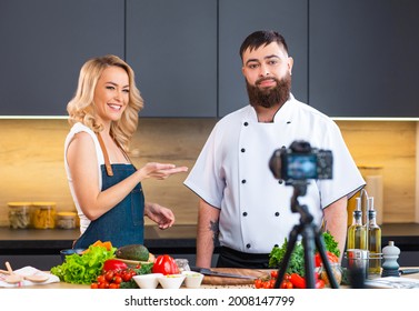 Young Woman And Man Prepare Food And Host A Cooking Show. The Bloggers Stream From Modern Kitchen. Healthy Food Preparation.