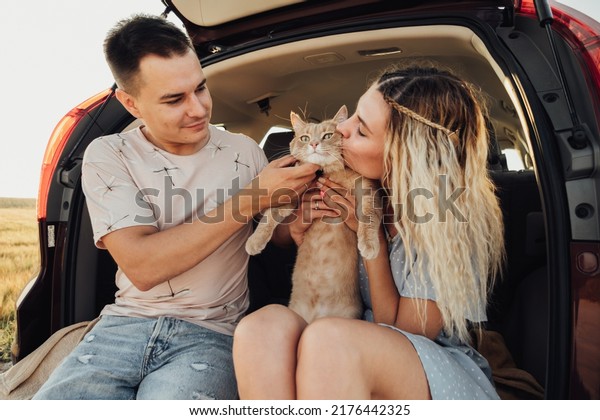Young Woman and Man\
Sitting in Trunk of Car with Pet, Happy Couple with Their Red Cat\
Enjoying Road Trip