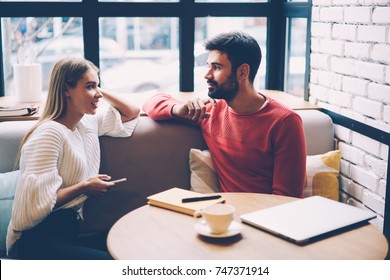 Young woman and man talking during first date in cozy coffee shop enjoying free time together,hipster girl checking notification on mobile while spending time with boyfriend having lovely conversation