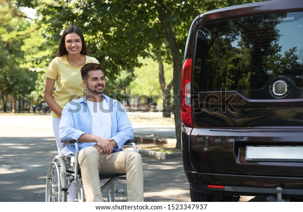 Young\
woman with man in wheelchair near van\
outdoors