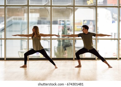 Young Woman And Man Working Out Indoors. Two People Doing Exercises. Warrior 2 Or Virabhadrasana II Pose. 