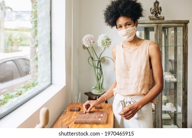 Young woman with mask arranging jewelry on wooden piece for display. Jewelry designer running business during pandemic. - Powered by Shutterstock