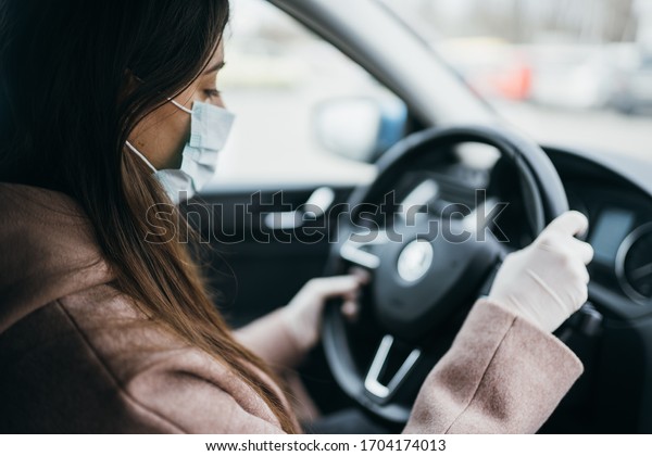 Young woman in\
a mask and gloves driving a\
car.