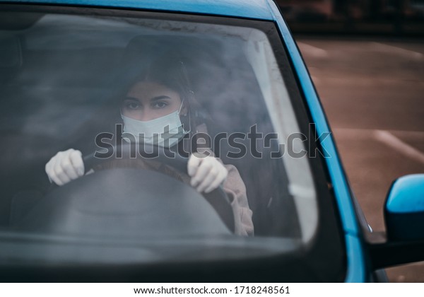 Young woman in\
a mask and gloves driving a\
car.