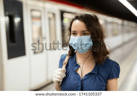 Young woman in mask and protective gloves waiting for subway train at underground station, enjoying favorite music on earphones. Concept of prevention and social distancing in coronavirus pandemic