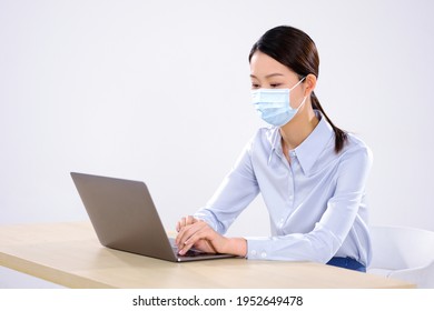 A Young Woman With A Mask Is Using A Laptop In The Office Not Looking At The Camera