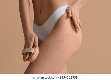 Young woman with massage brush scrubbing leg on beige background - Powered by Shutterstock