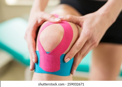 Young woman massage injured knee with kinesiotaping