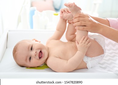 Young woman massaging cute baby on changing table