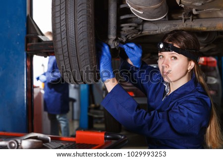 Young woman master is repairing car in workshop at workplace
