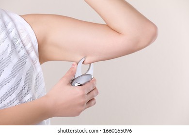 Young woman measuring body fat with caliper on beige background, closeup. Nutritionist's tool