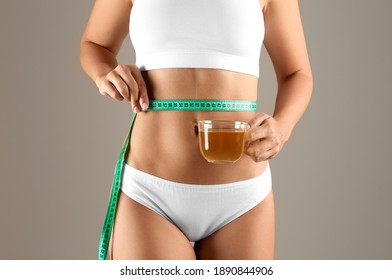 Young woman with measuring tape holding cup of diet tea on beige background, closeup