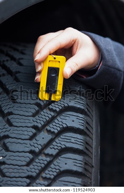 a young woman is measuring the tread depth of\
her car tire. the proper depth in the tread of a tire can prevent\
accidents.