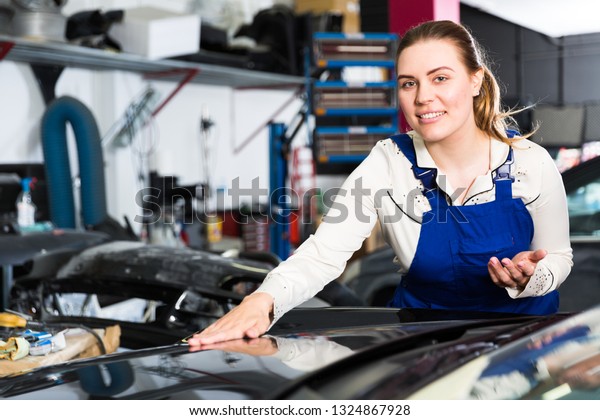 Young woman mechanic demonstrating repainted car in\
auto repair shop