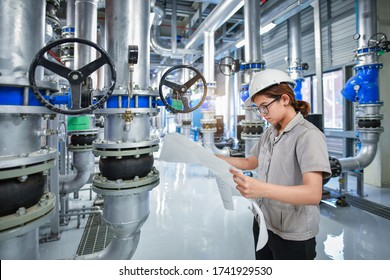 Young Woman Mechanical Engineer Holding Drawing To Checking And Inspection Of HVAC Heating Ventilation Air Conditioning System On Pressure Gauge Of Industrial Air Compressor Boiler Pump Room System
