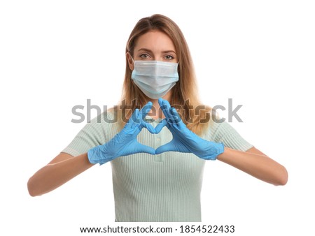 Young woman in medical gloves and protective mask making heart with hands on white background