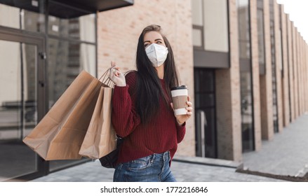 Young Woman In Medical Mask Walk Outdoors With Coffee Cup And Shopping Bags After Shopping