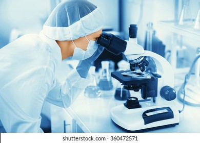 Young woman medical researcher looking through microscop slide in the life science (forensics, microbiology, biochemistry, genetics, oncology) laboratory. Medicine concept. 