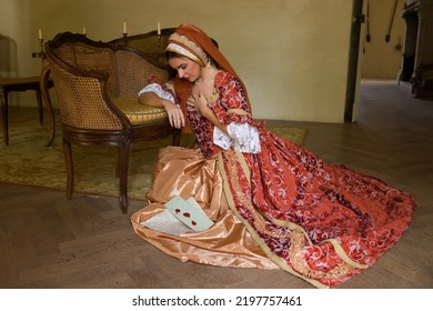 Young Woman In Medieval Renaissance Costume And French Hood Sitting On The Floor Holding A Letter