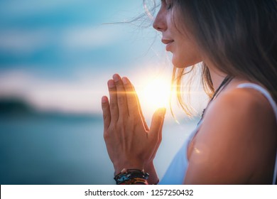 Jovem mulher meditando com os olhos fechados, praticando Yoga com as mãos em posição de oração.  