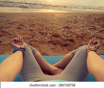 Young woman meditating in pose of lotus on beach at sunset in summer, point of view