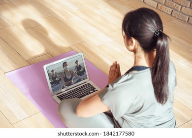 Young Woman Meditating Watching Live Online Tv Pilates Group Class Tutorial On Laptop Computer At Home Doing Yoga Virtual Training Fitness Workout Meditation Exercise Stream. Over Shoulder Screen View