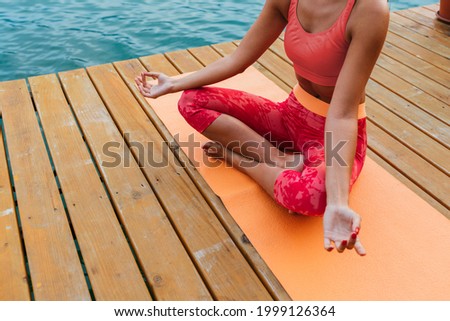 Young woman meditating at the wooden pier near lake during morning