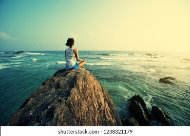 Young woman meditation on seaside rock cliff edge 