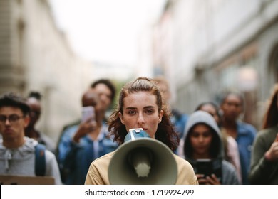 Young woman with a megaphone with group of demonstrator in background. Woman protesting with megaphone in the city. - Powered by Shutterstock