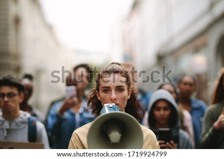 Young woman with a megaphone with group of demonstrator in background. Woman protesting with megaphone in the city.