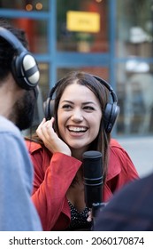 Young Woman With Microphone And Headphones Working Outside Conducting Recording Interview For Tv Or Radio Podcast. Female Digital Content Creator Working As A Journalist 