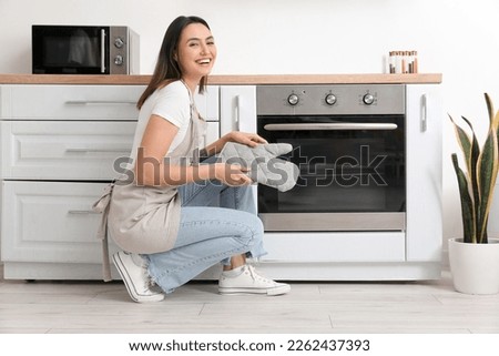 Young woman with mitten near electric oven in kitchen