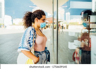 Young woman mixed race outdoors looking shop window - Woman shopping outdoors wearing surgical mask