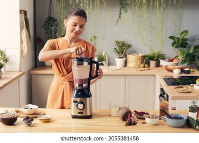 Young woman mixing ingredients of smoothie in electric blender while preparing healthy drink - Powered by Shutterstock