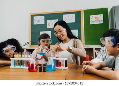 Young Woman Mixing Liquids In Test Tube With Multiethnic Children Watching, Learning About Science, Chemistry. Asian School Teacher And Students In Science Class