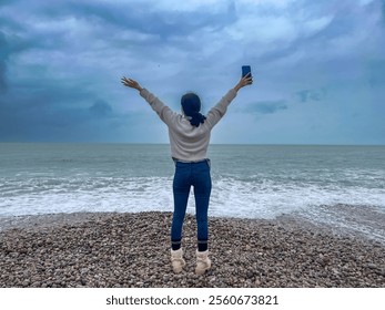 Young woman with mobile phone in her hands walking on the beach of the sea at Etretat, Normandy, France.  - Powered by Shutterstock