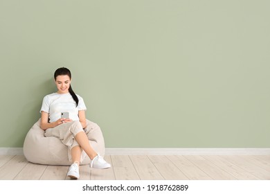 Young Woman With Mobile Phone Relaxing On Beanbag Near Color Wall