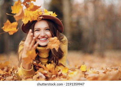 Young woman model lying in autumn park with yellow foliage maple leaves. Fall season fashion