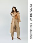 A young woman models a chic autumn outfit, featuring a stylish trench coat and tailored pants, exuding elegance in a studio.