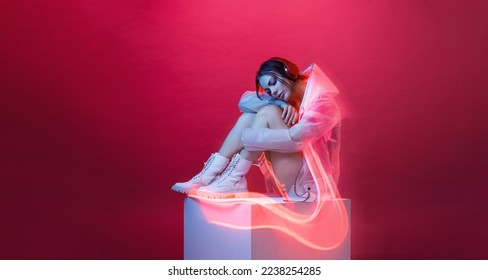 Young woman in modern headphones listens to music. Woman in futuristic costume. Augmented reality game, future technology, AI concept. VR. Neon red light. Viva magenta color of the year 2023.  - Powered by Shutterstock