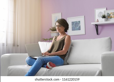 Young woman with modern laptop sitting on sofa at home - Shutterstock ID 1161220159