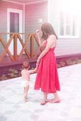 Young Woman Mom Walking With Baby Son Walking On The Street Joy Happy Smiling. Brunette In Red Dress Sunlight Lifestyle Blurred Background Copy Space