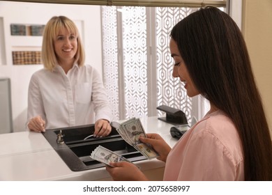 Young Woman With Money At Cash Department Window In Bank. Currency Exchange