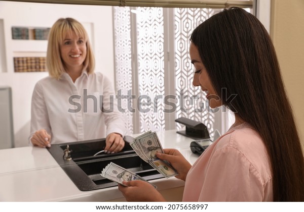 Young woman with money at cash department window\
in bank. Currency\
exchange