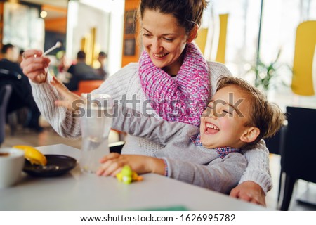 Young woman mother with small boy child son having fun at cafe or restaurant caucasian kid smiling while sitting by the table teasing playing