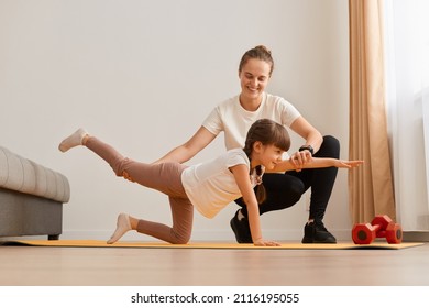Young woman mother teaching her daughter doing the exercises on all fours arching, back straightening, sport together at home, healthy kid's lifestyle, fitness involvement. - Powered by Shutterstock