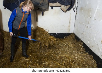 Young woman 'mucking out' cleaning horse stable. - Shutterstock ID 408233800